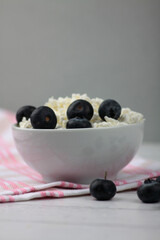 white bowl of farmer cheese on red and white napkin and a pile of blueberry on white wooden background flat lay. Healthy eating concept. Horizontal image