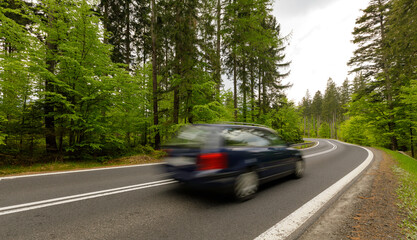 A winding mountain road through a green forest with a car riding