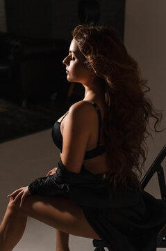 a girl with a magnificent hairstyle with curls and a make-up in a black erotic robe and underwear in a studio on a white background on a cyclorama