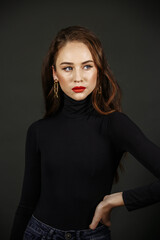 Naklejka premium A brunette in black clothes, with bright make-up, against the background of a dark wall