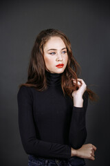 Naklejka premium A brunette in black clothes, with bright make-up, against the background of a dark wall