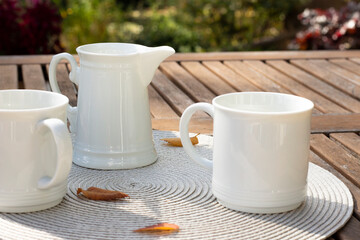 White jug with milk and cups on a wooden table. Breakfast on the veranda. Fresh drink, autumn leaves and oudoor. Close up photography
