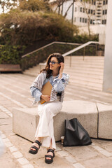 Positive young caucasian girl with notebooks resting sitting near campus during daytime. Brunette student is returning from university. Education concept