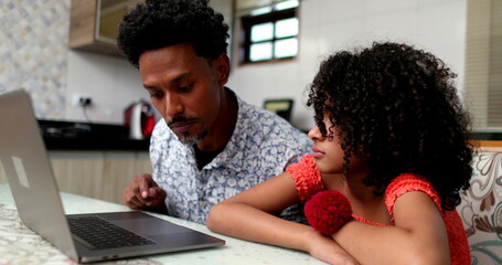 Black father helping daughter with computer laptop at home kitchen