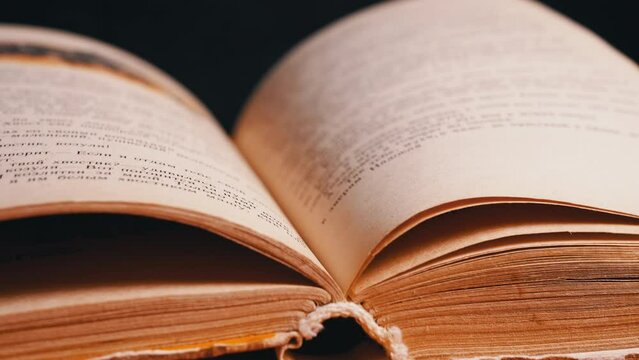 Female Fingers Leafing Through Pages of Old Shabby Book on a Black Background. Reading. Rough papyrus paper on a thick antique book from yesteryear. Orange color. Education. Knowledge. Mystic.