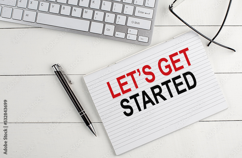 Poster let s get started text on notebook with keyboard , pen glasses on white wooden background