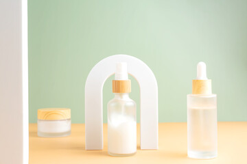 Beauty product concept. Jar of cream and bottles of serum on beige background in the arch. Front...