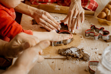 Side close up view of family member's hands cutting out different Christmas shapes out of raw dough to bake festive Christmas gingerbread cookies