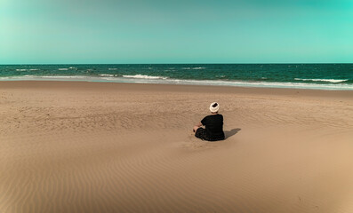 Fototapeta na wymiar Mature woman in turban resting on lonely beach. Copy space.