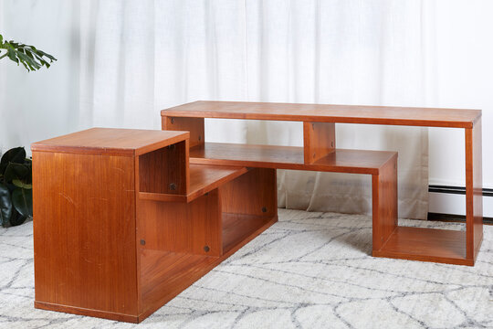 Unique Interlocking Puzzle Modular Teak Shelves Placed At An Angle  In Front Of White Drapes On Wood Floor	