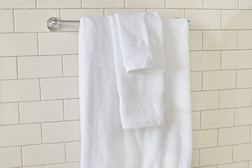 Soft clean white towels hanging in front of a luxurious tile wall. Silver metal towel bar rack.