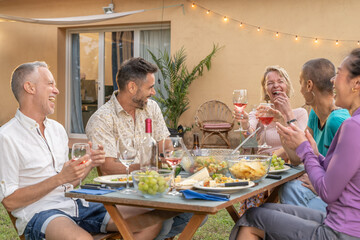 Multiethnic friends eating and drinking happy smiling and laughing in the patio. Middle-aged cheerful people around the table.