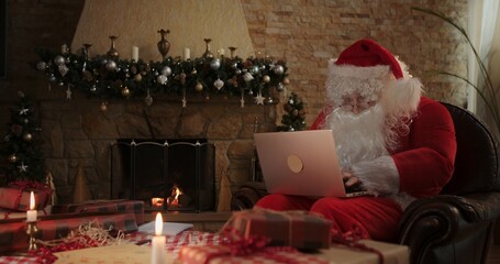 Cheerful Santa Claus checks letters in laptop on Christmas