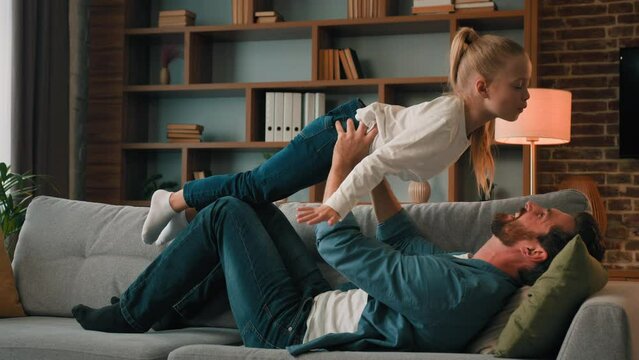 Happy child girl playing with father in children airplane game flying on parent arms having fun together at home young family doing acrobatic trick dad lifting up daughter funny kid enjoying activity