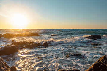 Beautiful seascape. Waves break on stone boulders on the seashore under the sunset sky