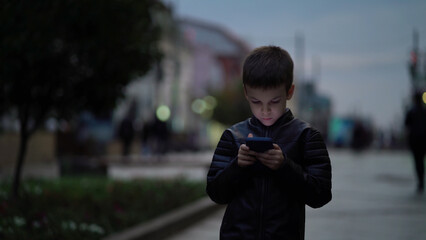 Child boy with a modern smartphone walks through the night city along the street - 532854043