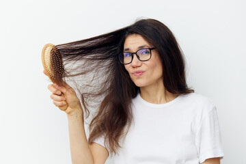 a beautiful, pleasant, sweet woman in eyeglasses and a white cotton T-shirt combs her long, well-groomed hair standing on a light background