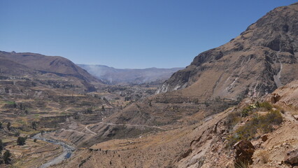 Fototapeta na wymiar Une route passant à travers de hautes montagnes, avec des champs d'agriculture en bas, traversée péruvienne, en plein jour, terre sec et rouge, orange