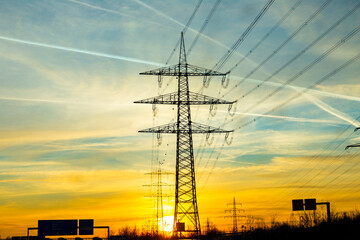  sunset seen from highway with electric pylon and condensation stripes from aircrafts at the sky - obrazy, fototapety, plakaty