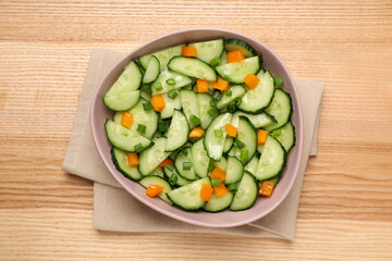 Tasty fresh salad with cucumber in bowl on wooden table, top view