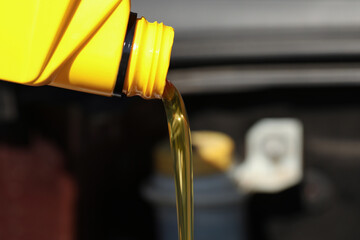 Pouring motor oil from yellow container against blurred background, closeup. Space for text