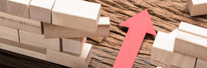 Red Paper Arrow Amidst Blocks On Wooden Table