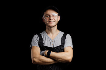 portrait of a working auto mechanic in glasses, a cap and overalls on a dark background.