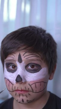 latin mother paints the face of her child son for the halloween celebration