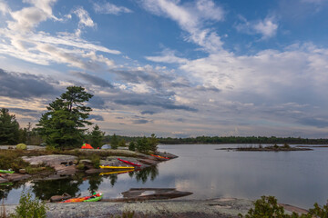 Sea kayaks and tents on a rocky shore by reflective water in Killarney Provincial Park. Shot in the...