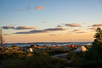 Tents set up on the smooth rock of Georgian Bay seen as the sunset turns clouds pink and blue over the water in the background.  Room for text.