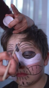 latin mother paints the face of her child for the halloween celebration