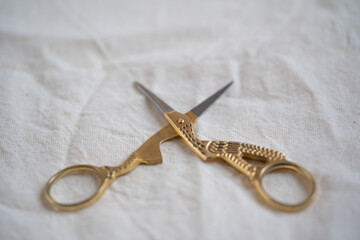 tijeras para cortar hilo en forma de cigüeña doradas sobre fondo de tela manta beige con espacio...