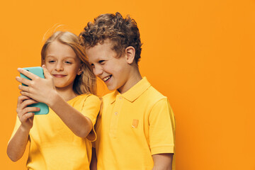 cute, funny children, school age, brother and sister stand on a yellow background and look into their smartphone
