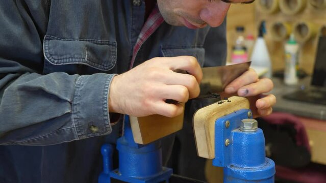 Professional guitar maker scraping ebony armrest for resonator guitar build in a workshop