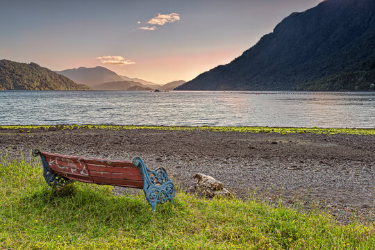 Bench on the beach near the town of Hornopiren with a peaceful view on the Comau fjord at sunset. The Comau fjord, also known as Leptepu, penetrates the mainland of Chile, in Los Lagos Region.