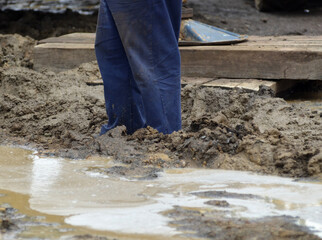 The lower legs of a worker on a muddy site during maintenance and construction.