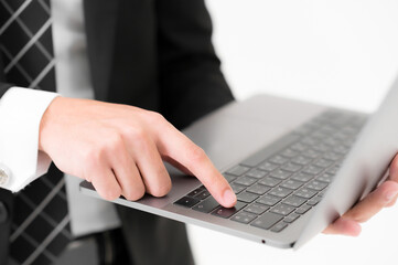 Close-up of Young Asian handsome hands using laptop checking smartphone, wearing a black suit on white background.