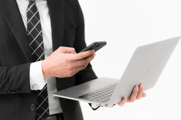 Close-up of Young Asian handsome hands using laptop checking smartphone, wearing a black suit on white background.