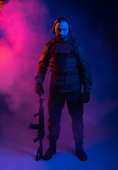 Fototapeta premium soldier in the studio on a blue background. a man in military uniform with a rifle or machine gun in colored light and smoke. military or airball player. blur