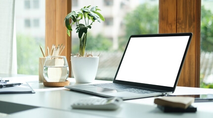 Comfortable home office. Laptop computer, stationery and potted plant on white table.