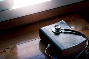 Stethoscope and the Bible on wooden table with light in the morning, concept for treatment, science and religion, with copy space , space for text.