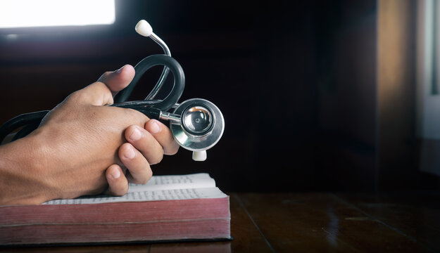 Hands holding stethoscope and the Bible and pray for healing, concept for treatment, science and religion, close up hands praying, with copy space , space for text.