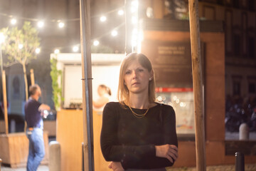 A young attractive woman stands by the stalls in the square at night. Soft focus and bokeh.