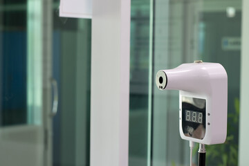 Automatic infrared thermometer with digital display for contactless temperature screening in modern office building, essential for health and safety during pandemic or workplace entrance control