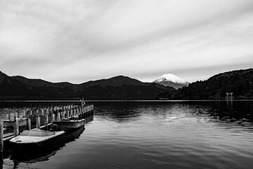 Obraz premium High contrast reflection of snow capped Mount Fuji in black and white with a pier, boats, and torii gate from Lake Ashi Hakone Japan