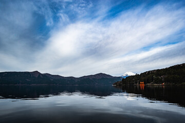 Reflection of snow capped Mount Fuji with a pier, boats, and torii gate from Lake Ashi Hakone Japan