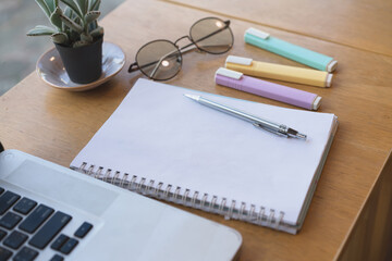 Writing on a notepad while working from home. A lap top  and plant are also on display on this brown striped working table. 