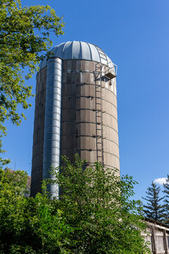 Landscape texture view of a rustic old concrete silo wall with blue sky background, showing natural weathering from age, framed by trees