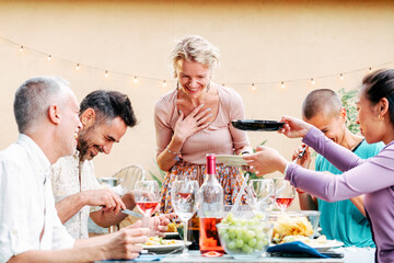 A group of adult friends sharing food in a barbeque party meeting with a lot of food and drink at...