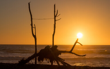 estructura de palos en playa al atardecer, con sol de fondo naranjo 